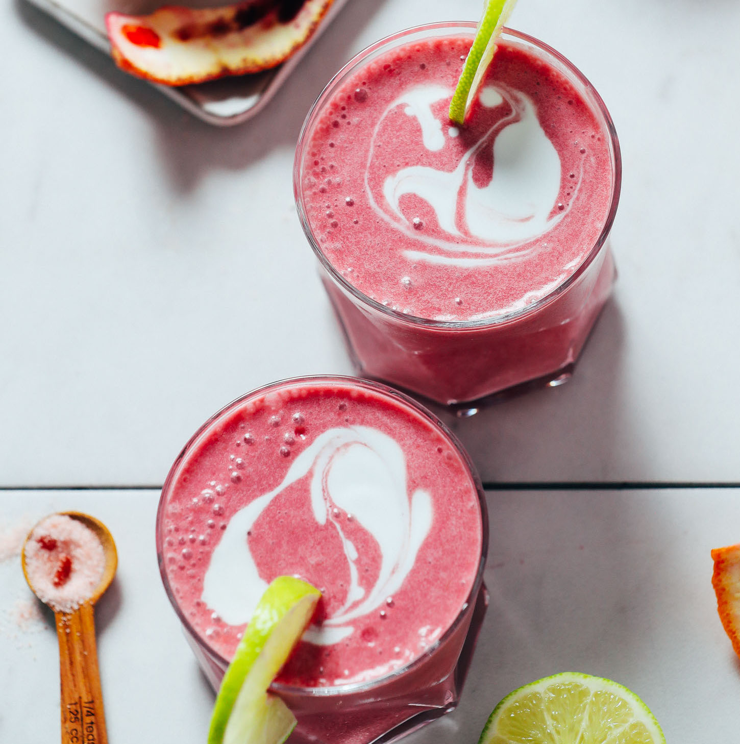 Top down shot of two glasses of Blood Orange Creamsicle Smoothies topped with coconut milk and lime slices