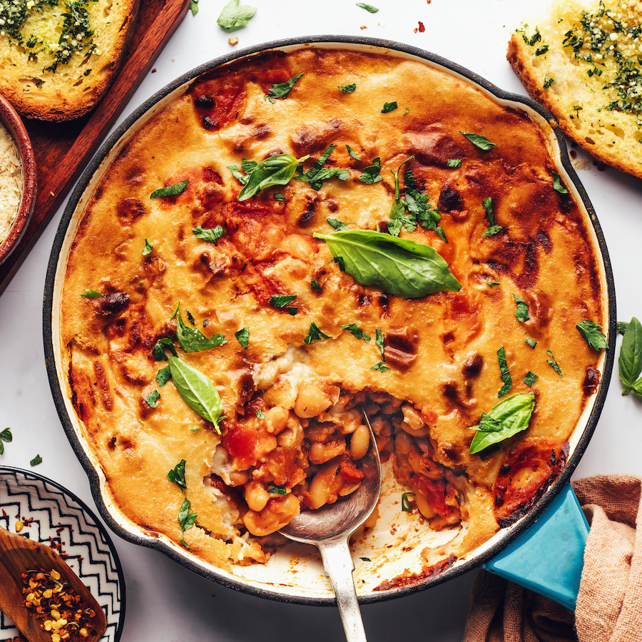 Cast iron pan of cheesy vegan pizza beans topped with fresh basil