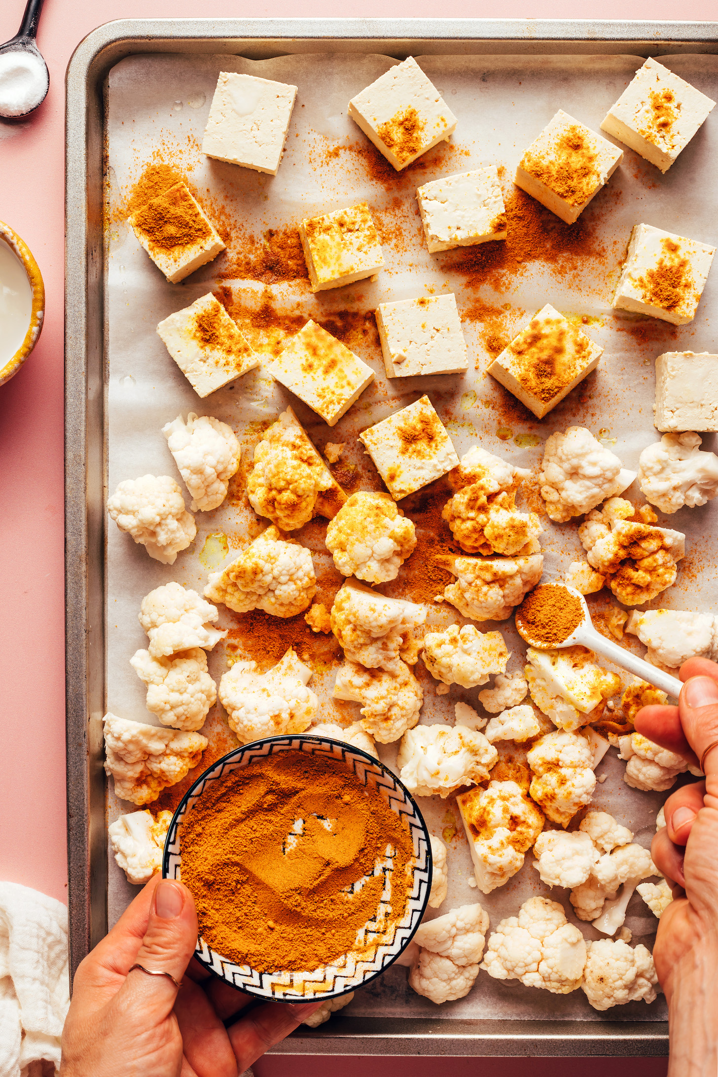 Sprinkling cubed tofu and cauliflower florets with curry powder