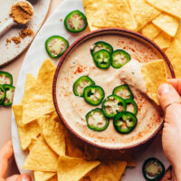 Dipping a tortilla chip into a bowl of vegan white bean queso