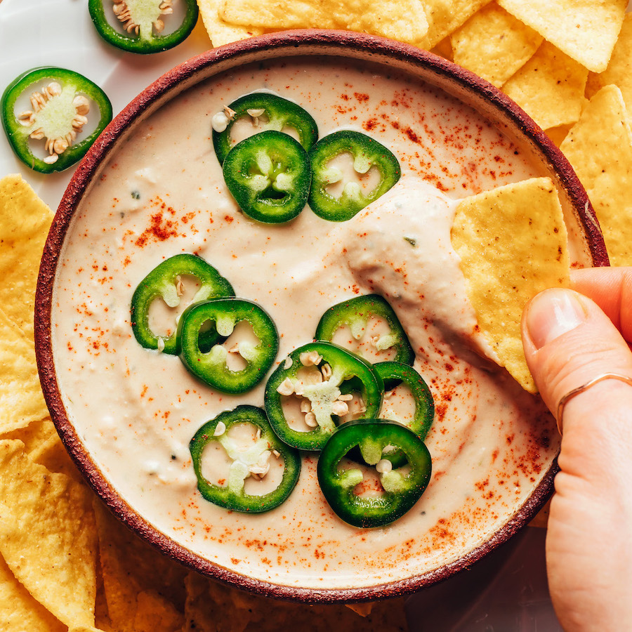 Dipping a tortilla chip into a bowl of vegan white bean queso