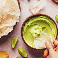 Dipping a crispy homemade rice paper chip into a bowl of vegan avocado dip