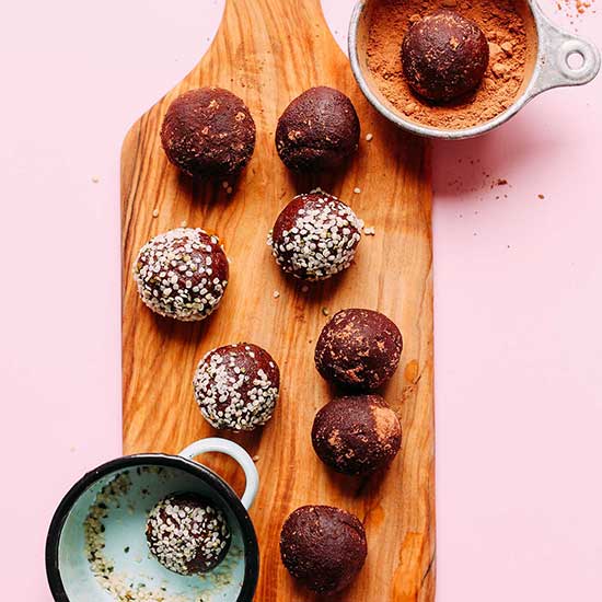 Cutting board of Dark Chocolate Hemp Energy Bites with some coated in hemp seeds and others in cacao powder