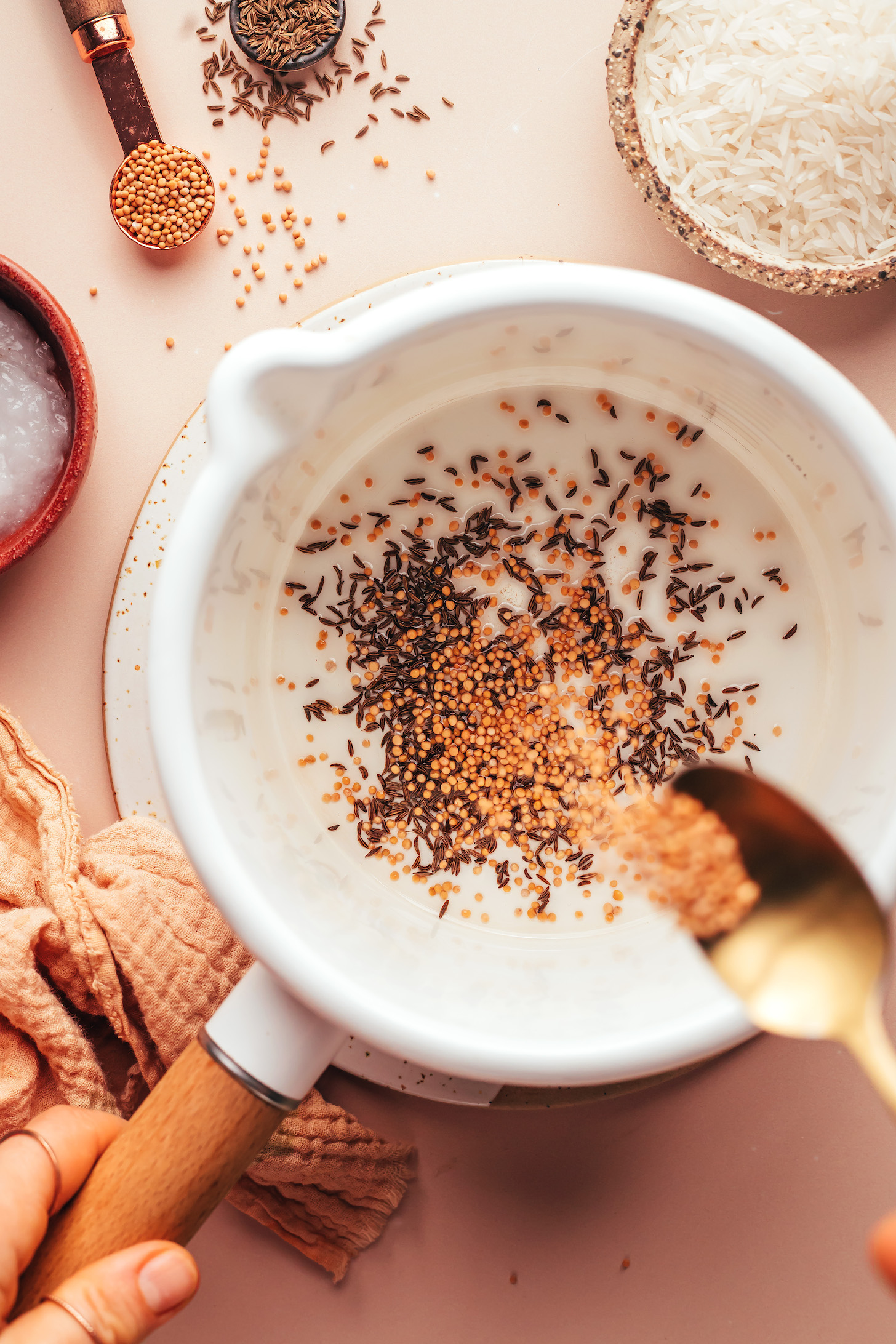 Sprinkling mustard seeds into a saucepan of melted coconut oil and cumin seeds