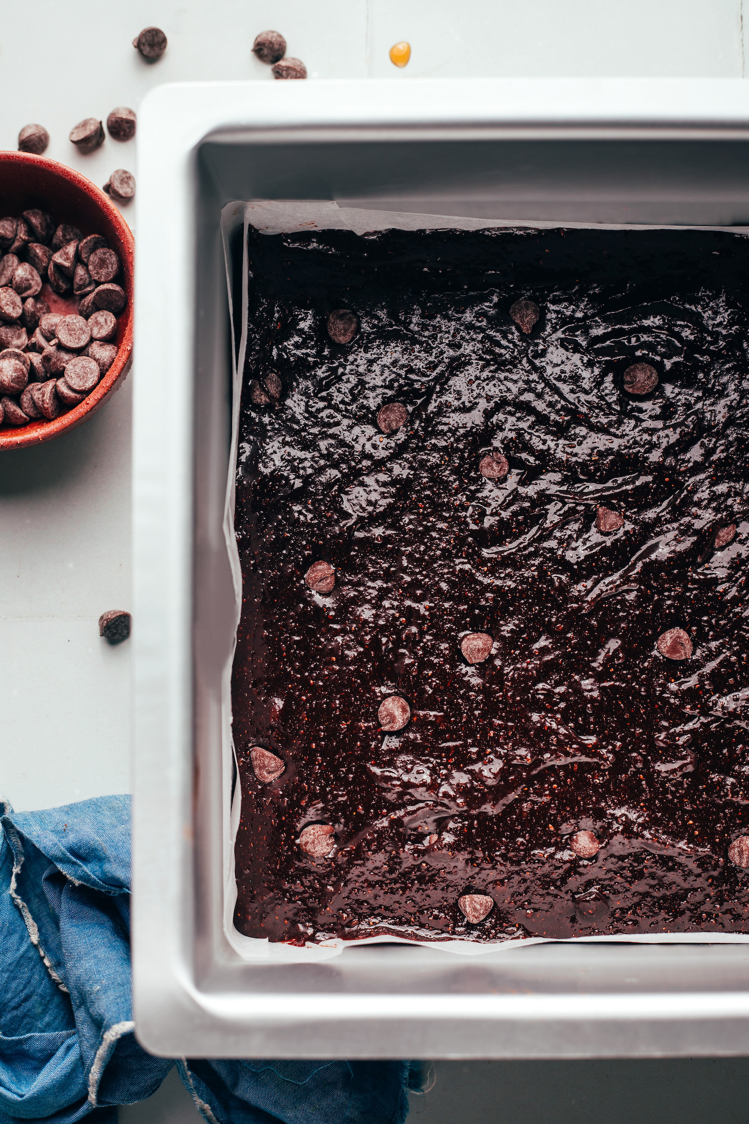 Bowl of chocolate chips next to a pan of brownie batter dappled with chocolate chips