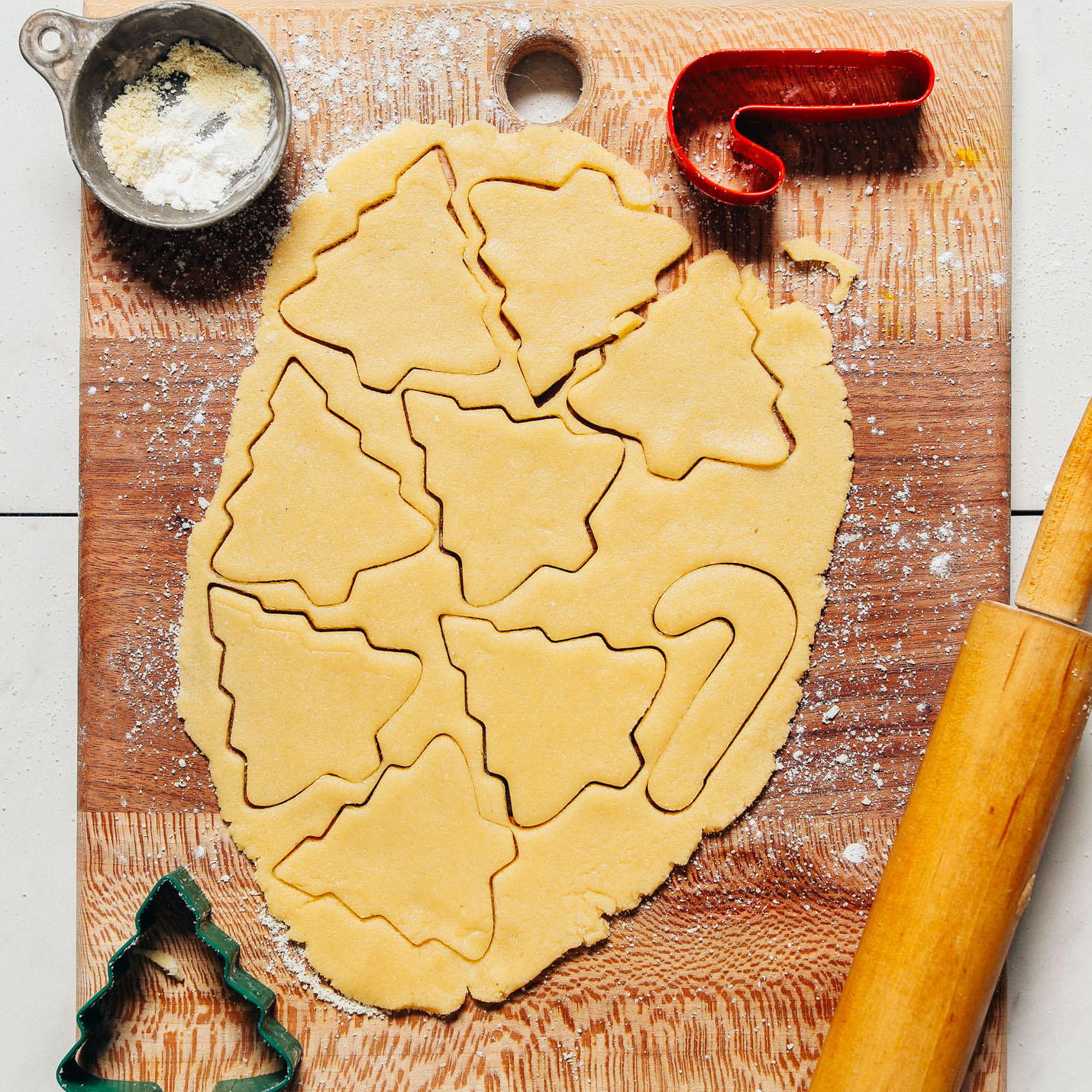 Cutting board with Grain-Free Sugar Cookie Dough cut into trees and a candy cane