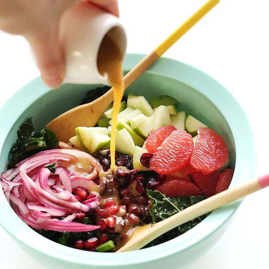 Pouring Red Wine Vinaigrette onto a big bowl of Kale Citrus Salad