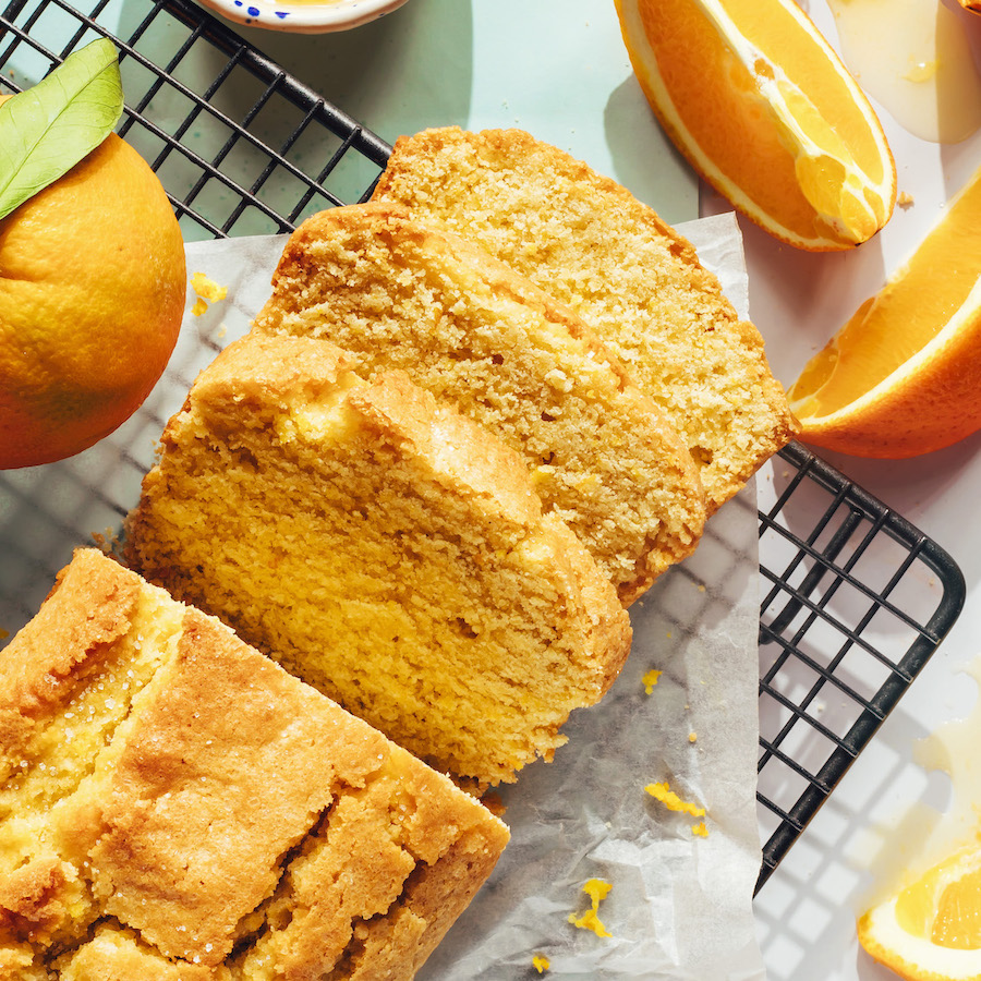 Fresh oranges around a partially sliced orange almond loaf cake