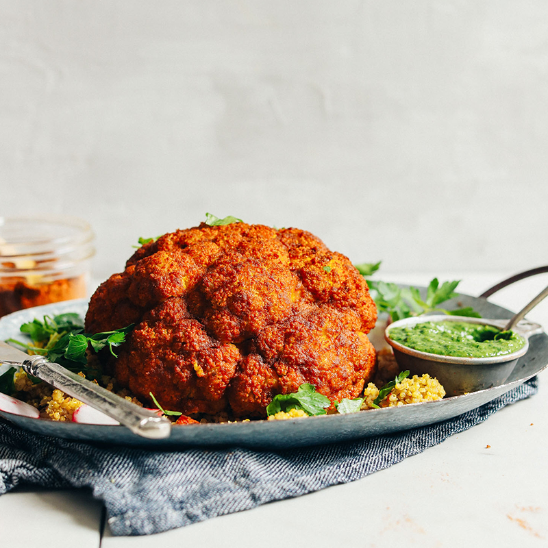 Platter filled with our Whole Roasted Cauliflower recipe served over quinoa with a side of green sauce