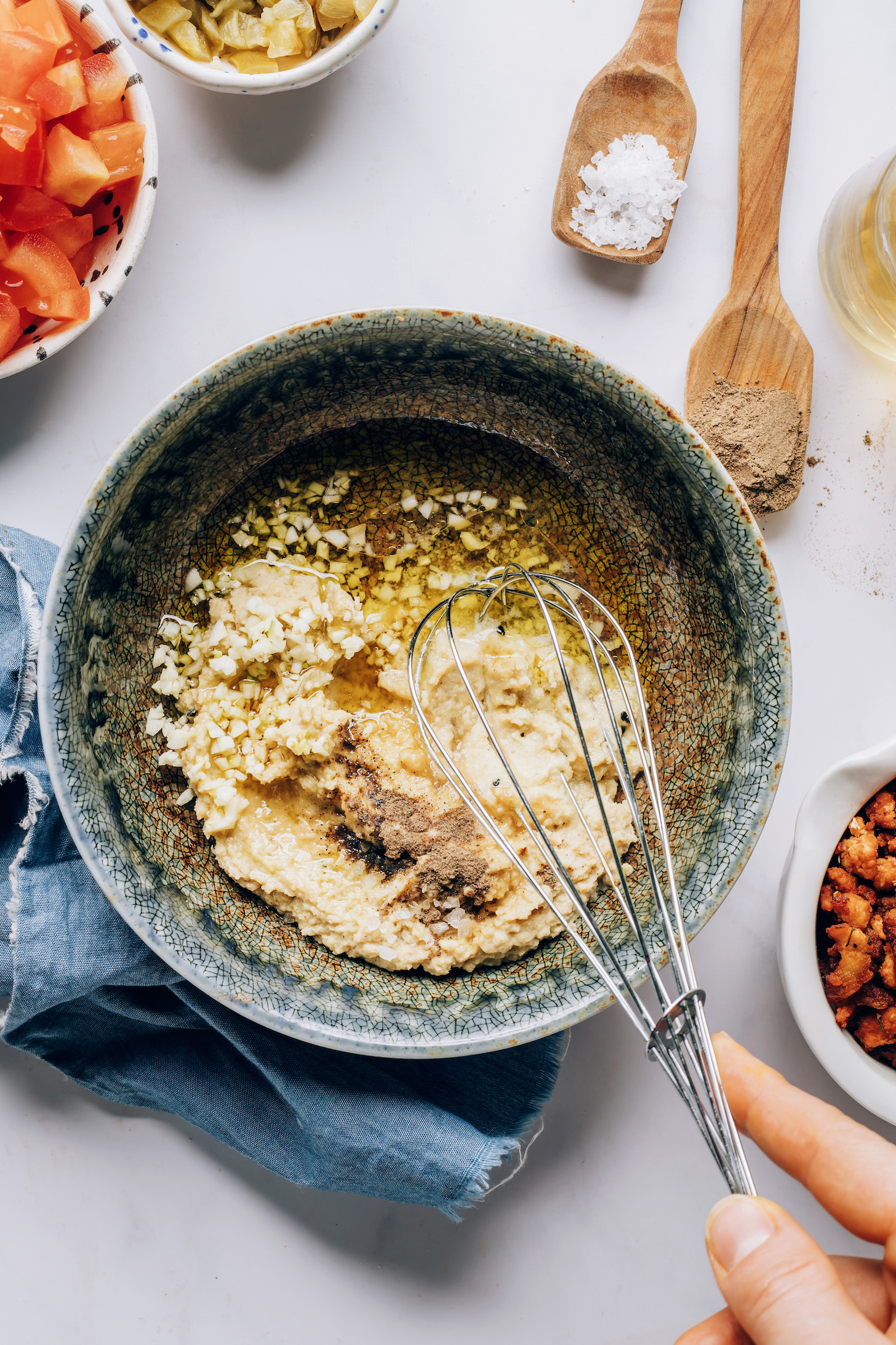 Whisking hummus, garlic, olive oil, apple cider vinegar, salt, and pepper to make a quick sauce