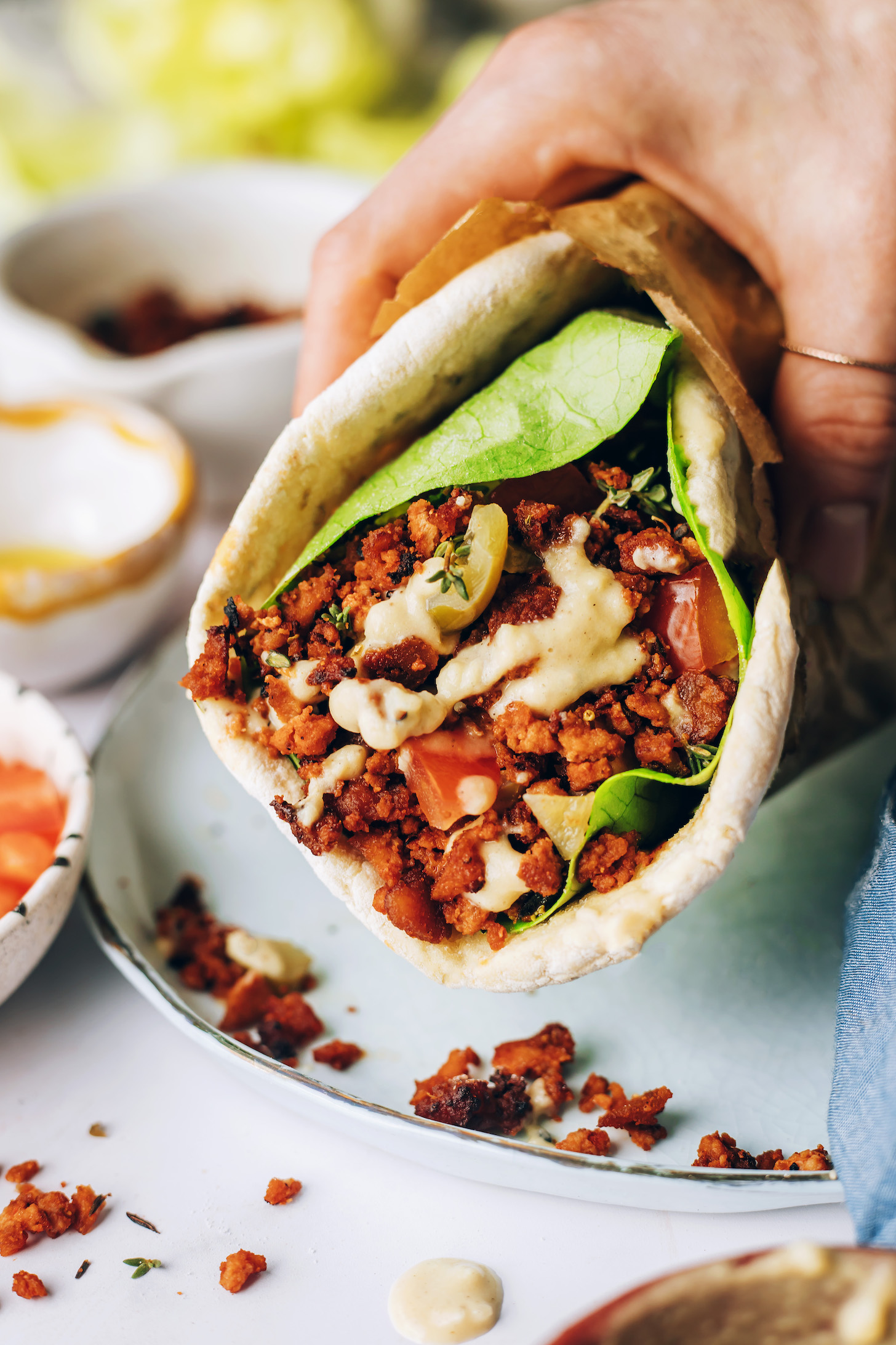 Holding a plant-based pita wrap stuffed with baked tofu, hummus sauce, lettuce, and tomatoes