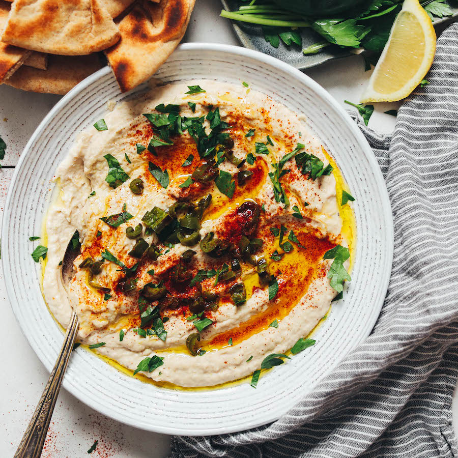 Vintage spoon in a bowl of white bean dip topped with serrano peppers