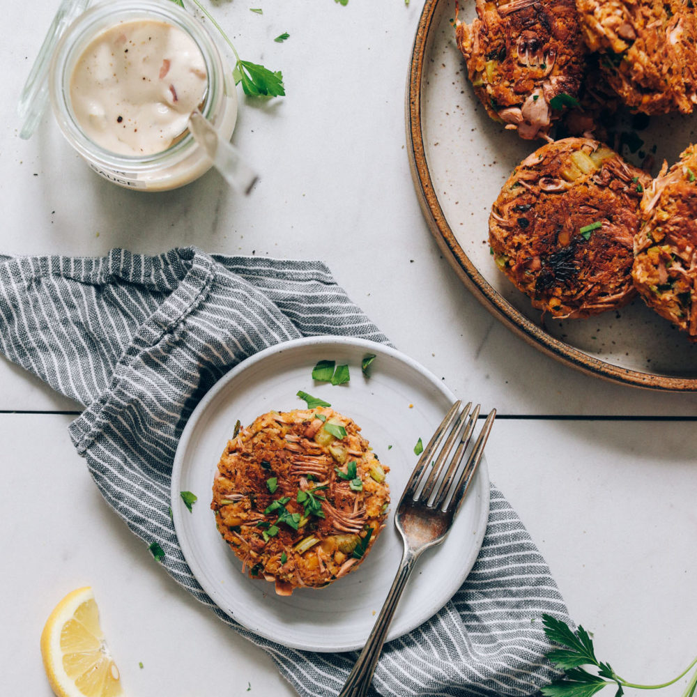 Two plates with vegan crab cakes next to a jar of vegan tartar sauce