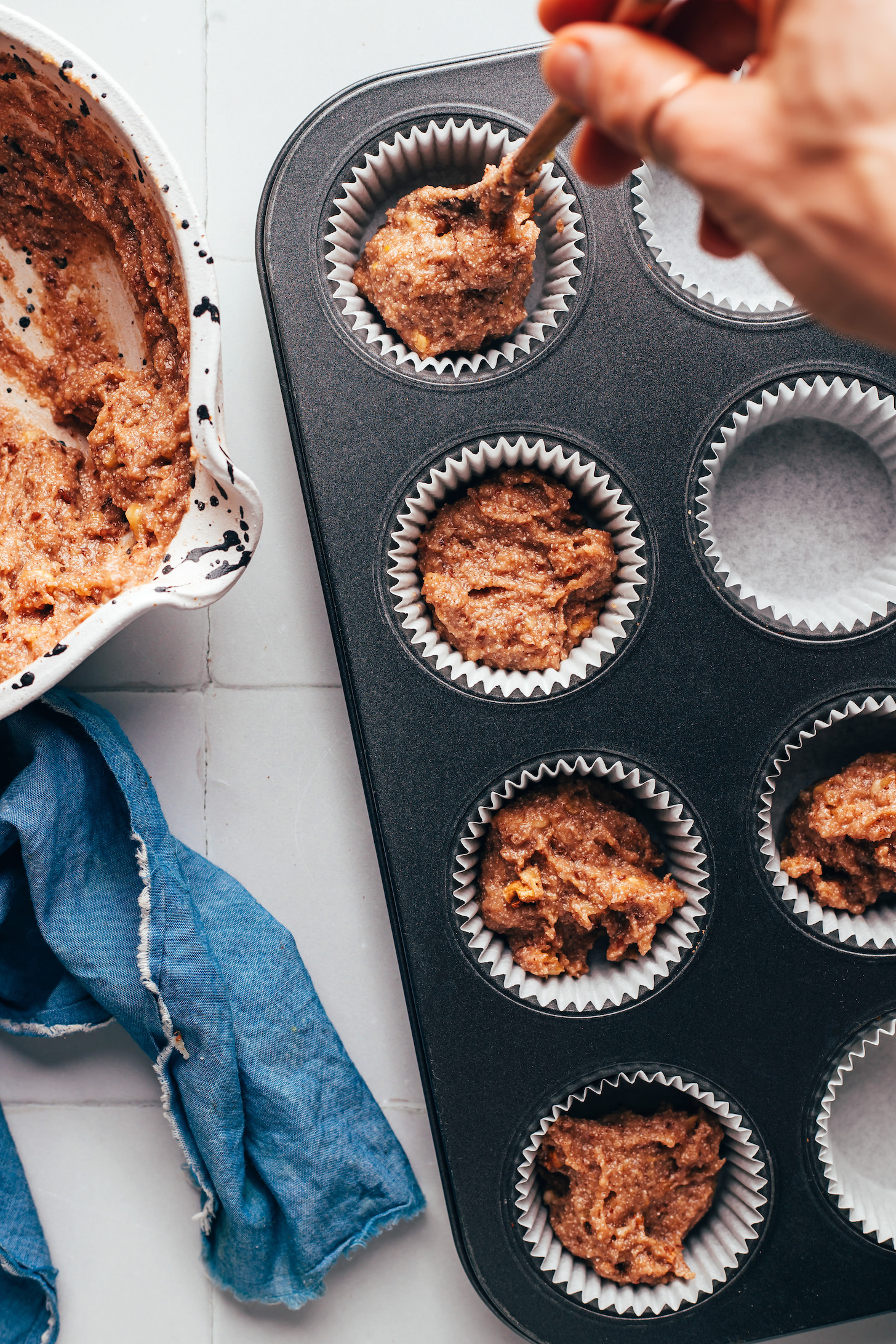 Using a spoon to add muffin batter to a lined muffin tin