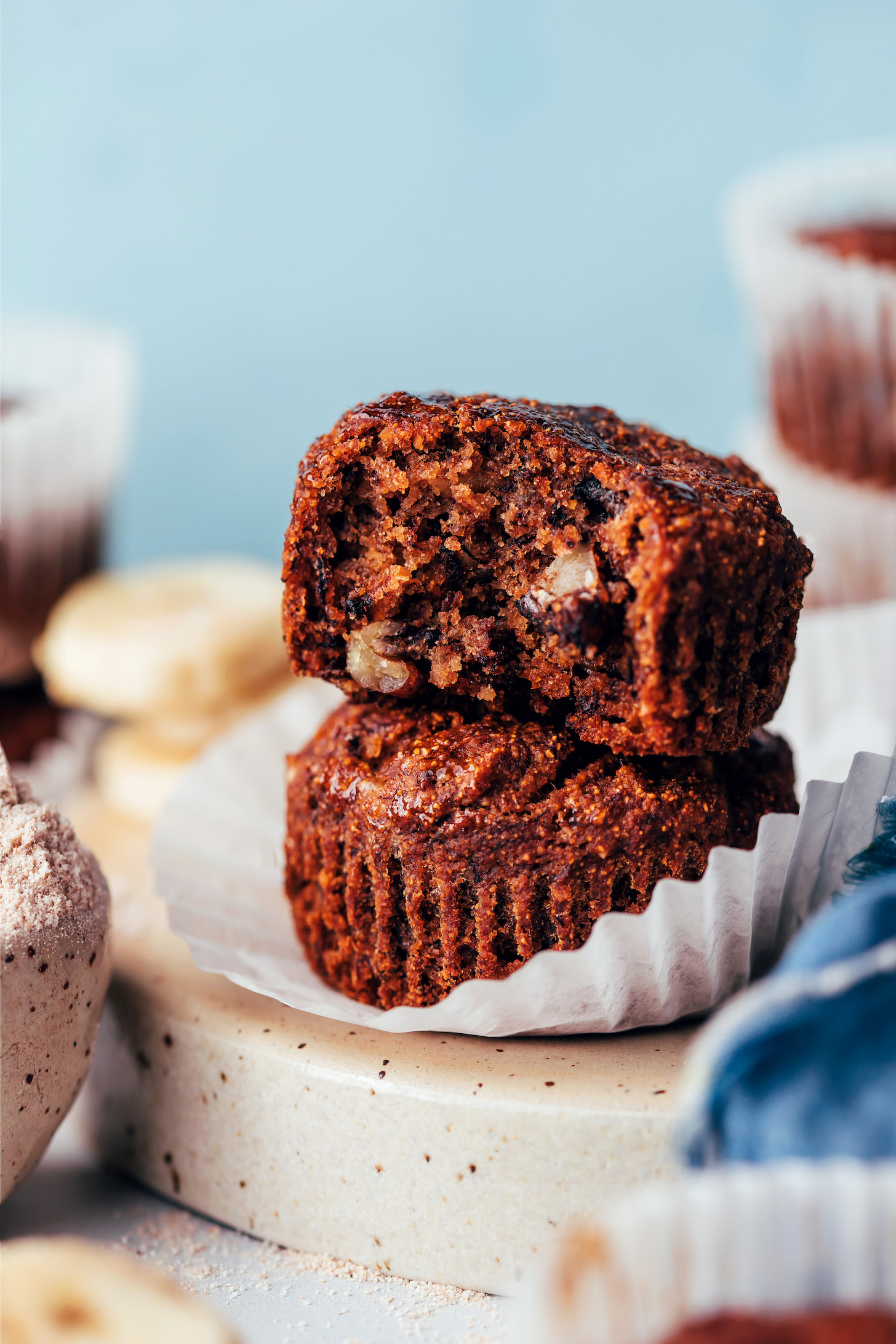 Two banana buckwheat muffins on a paper liner with the first one partially eaten to show the fluffy crumb texture