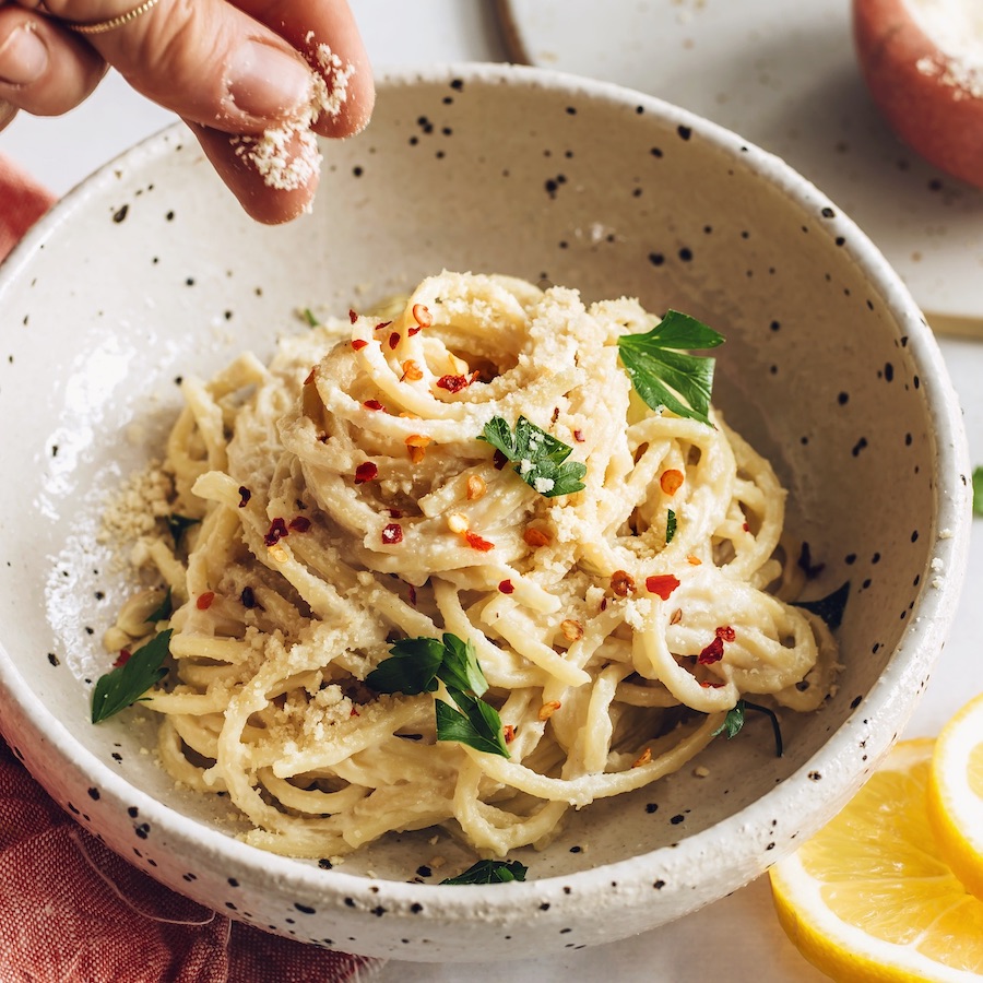 Sprinkling vegan parmesan cheese over a bowl of pasta al limone