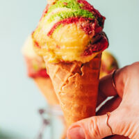 Hand holding a cone with a scoop of vegan rainbow sherbet ice cream on top