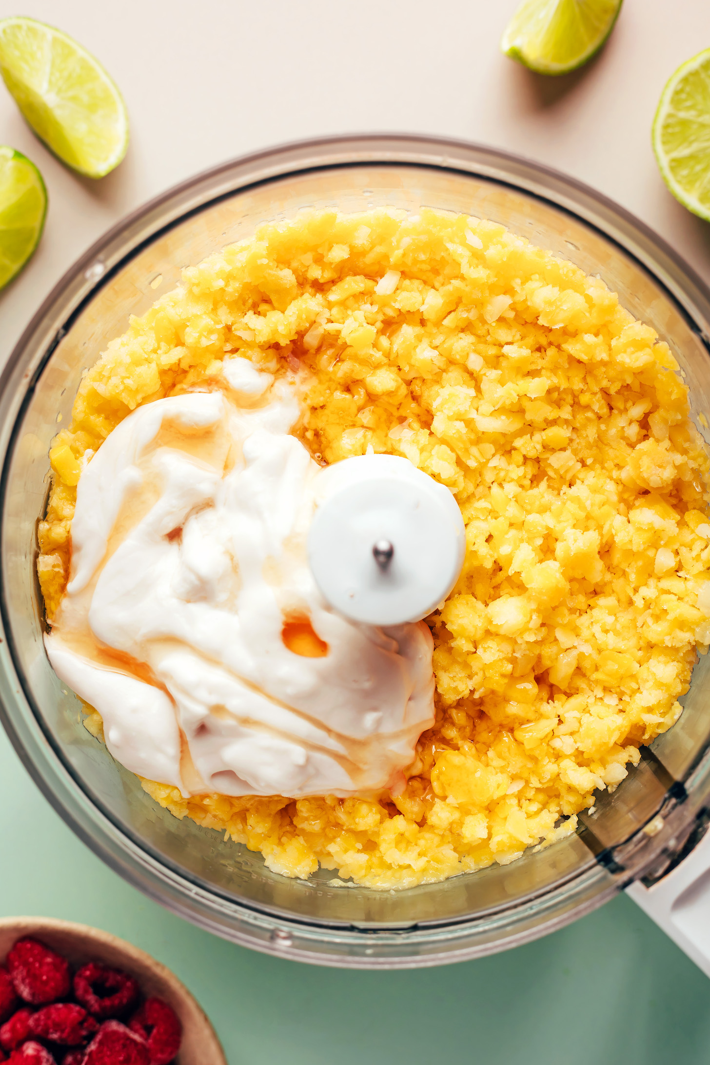 Food processor with frozen mango and pineapple blended into small pieces with coconut milk and maple syrup